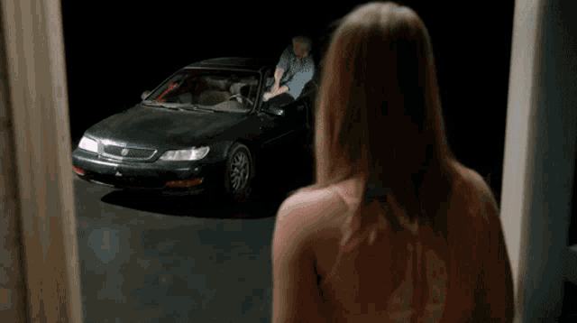 a woman in a pink tank top looks at a man in a black car