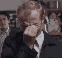 a man in a suit and tie is crying with his hand on his face .