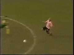 a man in a pink shirt is laying on the ground in front of a goalie