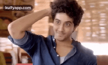 a young man with curly hair is holding his hand to his head .