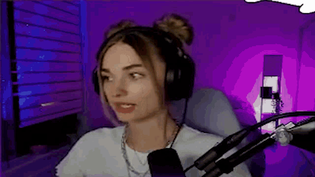 a woman wearing headphones is sitting in front of a microphone in a purple room .
