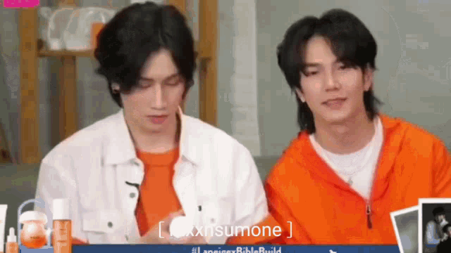 two young men are sitting next to each other in front of a bottle of lotion .