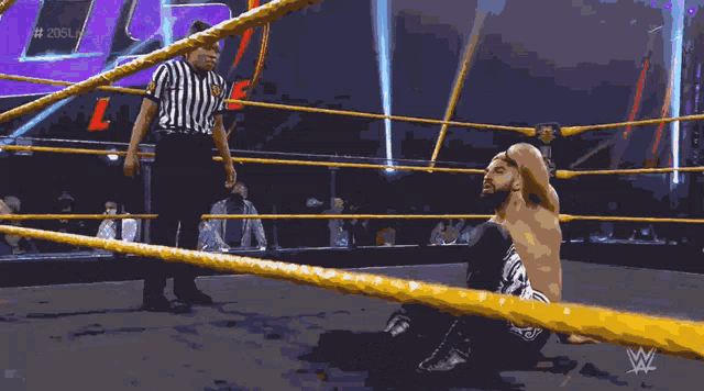 a wrestler is kneeling down in a wrestling ring while a referee watches