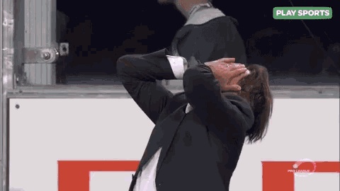 a man in a suit is covering his face with his hands in front of a play sports sign .