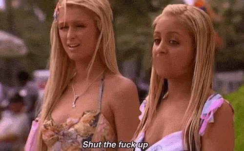 two blonde women are standing next to each other and one is saying `` shut the fuck up '' .