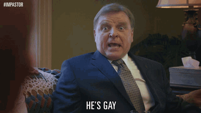 a man in a suit and tie says he 's gay with his finger