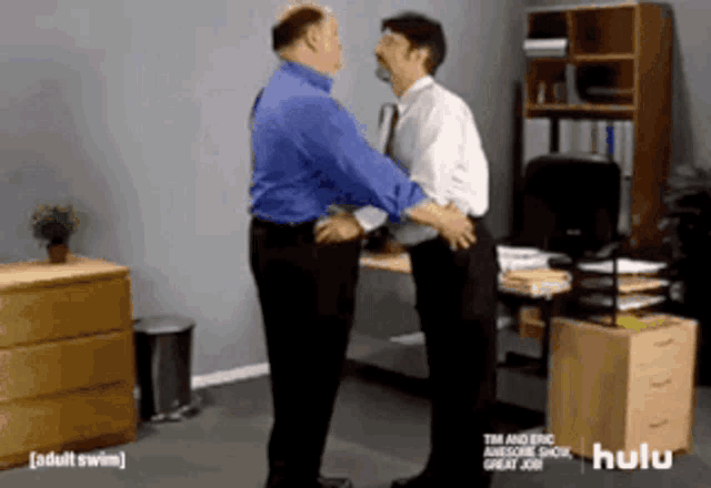 two men are standing in an office with hulu written on the bottom right