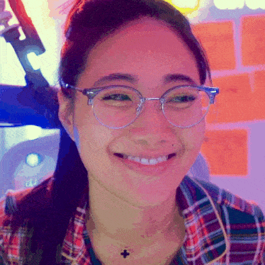 a girl wearing glasses and a plaid shirt smiles for the camera