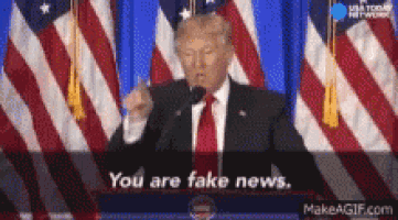 donald trump is giving a speech in front of an american flag and says you are fake news