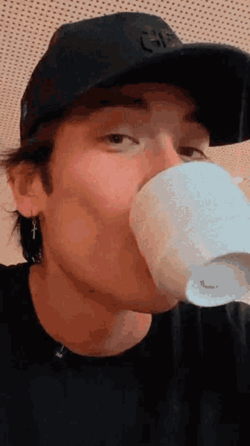 a man wearing a black hat and earrings is drinking from a white cup