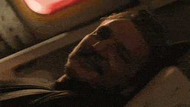 a man with a beard is laying in a dark room with a red light behind him