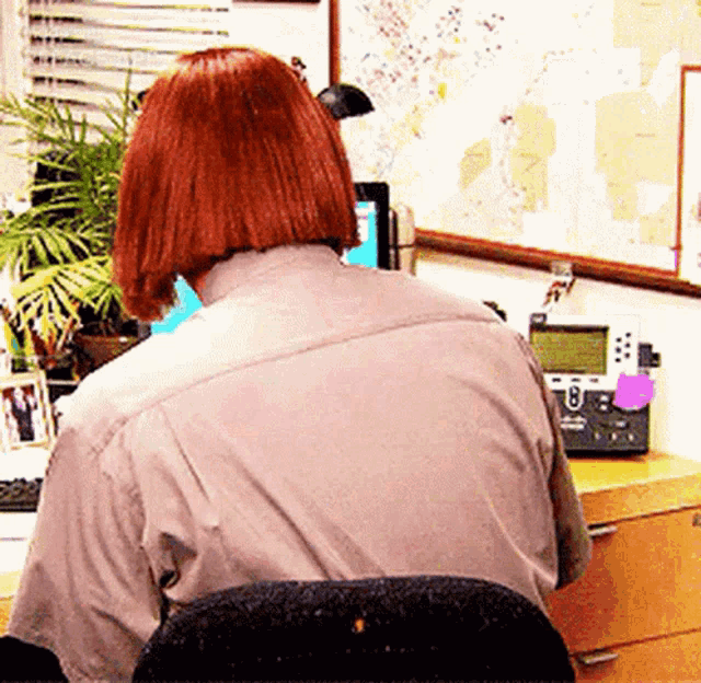 a woman with red hair is sitting at a desk with a telephone and a computer