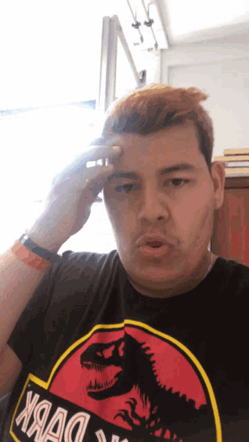 a man wearing a jurassic park t-shirt holds his head