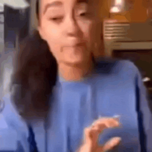 a woman in a blue sweater is making a funny face while talking on a video call .