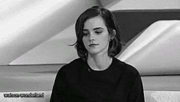 a black and white photo of a woman sitting on a couch looking at the camera .