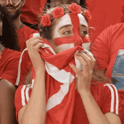 a woman with red paint on her face is covering her mouth with a scarf .