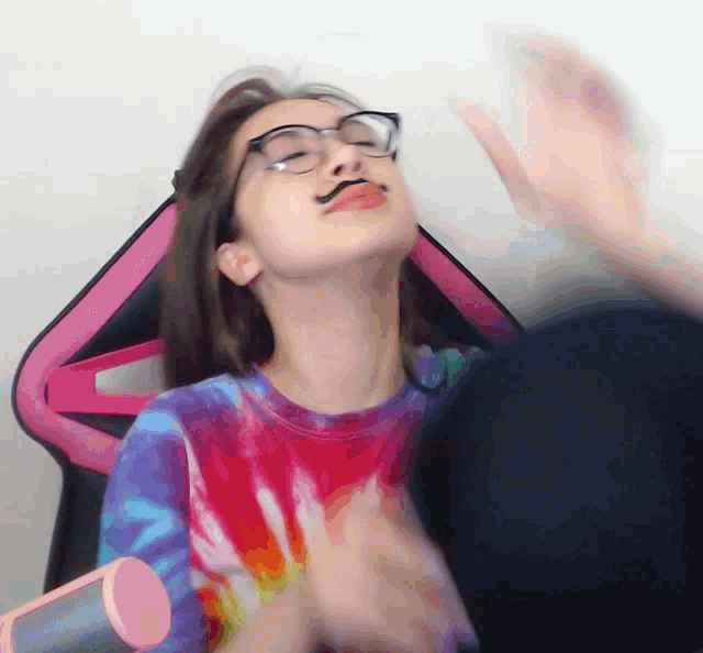 a girl wearing glasses and a tie dye shirt is sitting in a chair