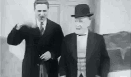 two men in suits and hats are standing next to each other in a room in a black and white photo .