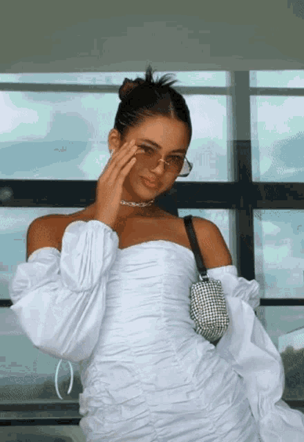 a woman wearing a white off the shoulder dress holds a purse