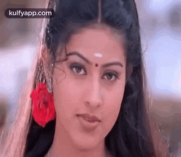 a close up of a woman 's face with a red flower in her hair and a bindi on her forehead .