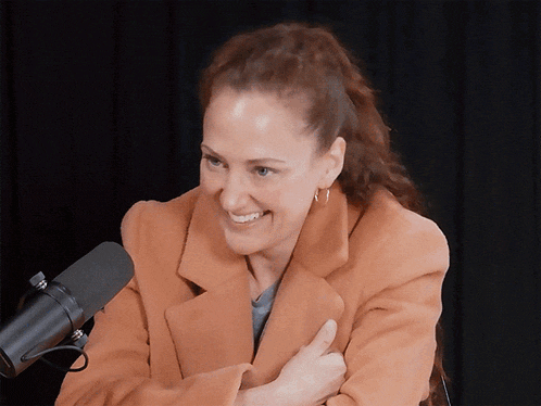 a woman in an orange coat is smiling in front of a black microphone