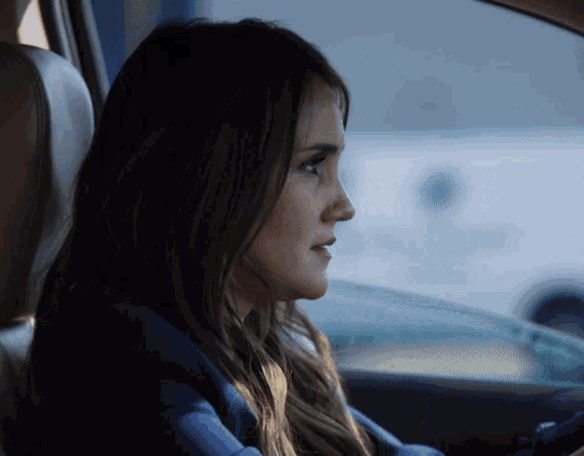 a woman in a blue jacket is sitting in the driver 's seat of a car