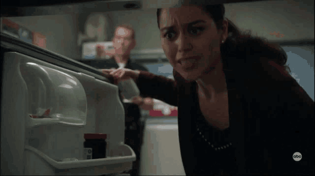 a woman is reaching into a refrigerator with a bottle of pills in it