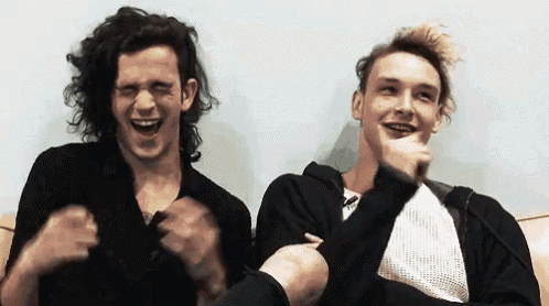 two young men are sitting next to each other on a couch laughing and making funny faces .