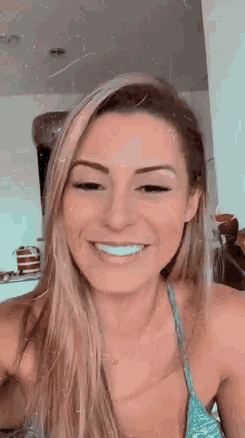 a woman in a bikini is smiling and looking at the camera while sitting in a kitchen .