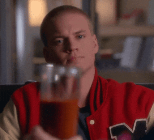 a man wearing a red jacket with the letter m on it holds a glass