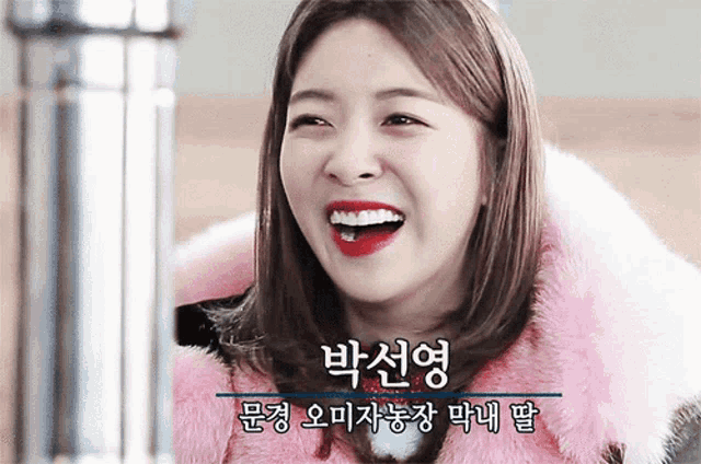 a woman wearing a pink fur coat is smiling with chinese writing behind her