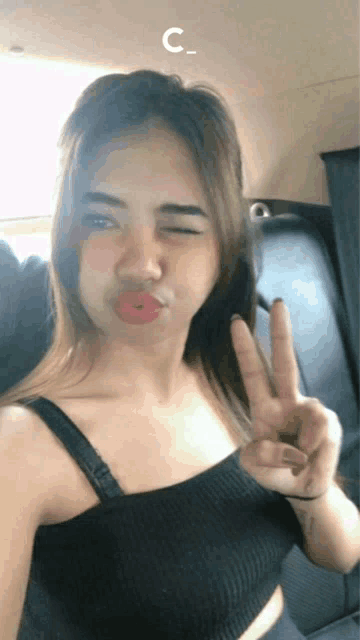 a woman in a black tank top winks and shows a peace sign