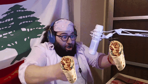 a man holding two burritos in front of a microphone with a flag in the background