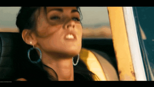 a woman wearing hoop earrings is sitting in a car with her eyes closed
