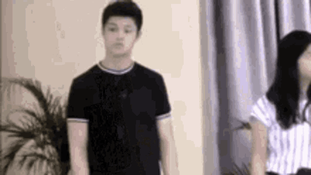 a man and a woman are standing next to each other in a living room . the woman is wearing a striped shirt .
