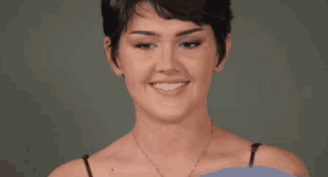 a woman with short hair is smiling and wearing a gold necklace
