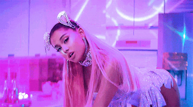 ariana grande is wearing a white dress and a tiara with rhinestones on her head .