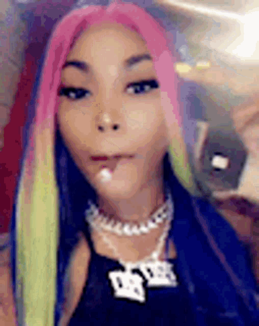 a woman with pink , green and blue hair is wearing a necklace and a black top .