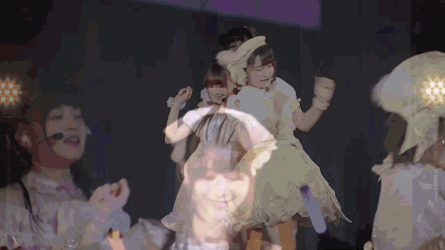 a group of girls are dancing on a stage with a projection of their faces
