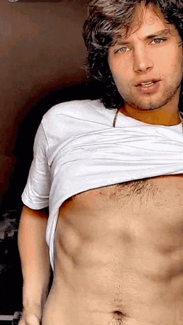 a shirtless man with a beard and green eyes is taking off his shirt