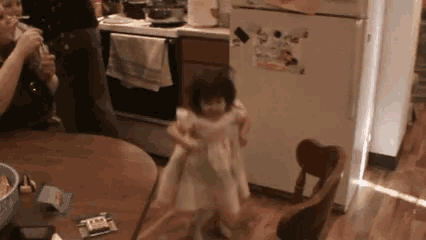 a little girl is dancing in a kitchen while a man drinks wine .