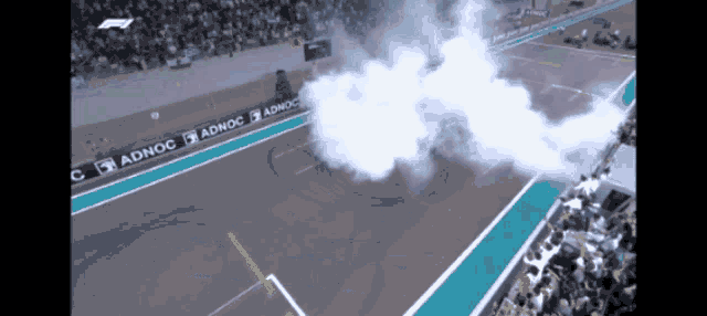 smoke is coming out of a race track with ads for adnoc on the side
