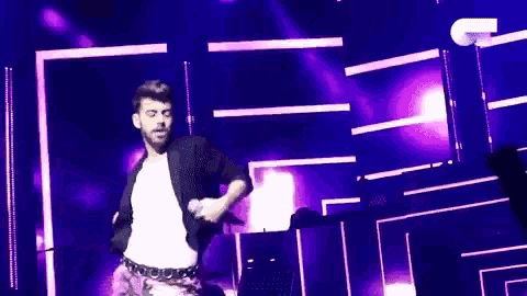 a man is singing into a microphone on a stage in front of purple lights .
