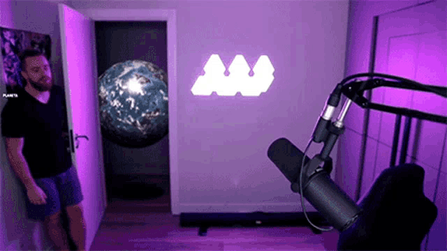 a man is standing in front of a microphone in a room with a planets logo on the wall