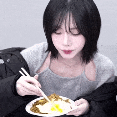 a woman is eating noodles with chopsticks from a white plate