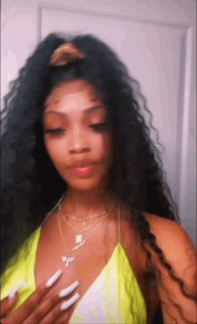 a woman with long black hair and white nails is wearing a neon yellow top and a necklace .