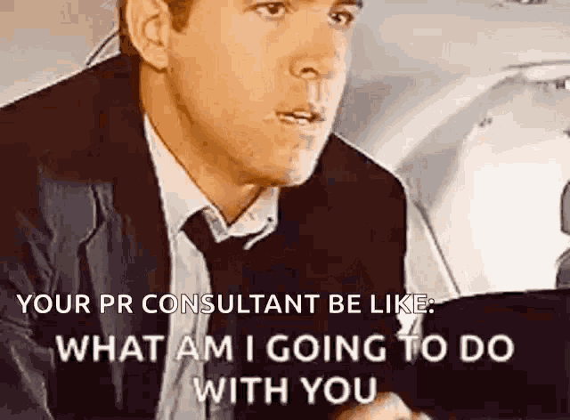 a man in a suit and tie is talking to another man while holding a tablet .