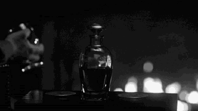 a black and white photo of a bottle of perfume and a glass of wine .