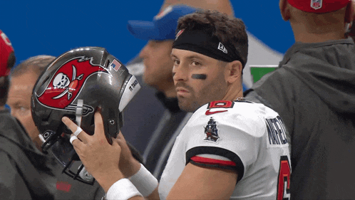 a man in a buccaneers jersey holds his helmet up