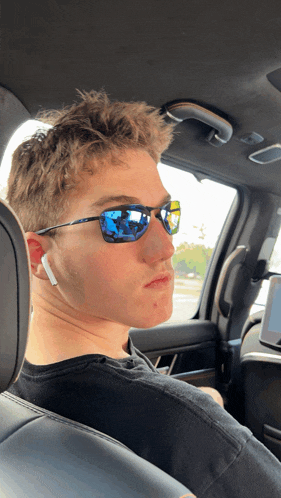 a young man wearing sunglasses and ear buds is sitting in a car